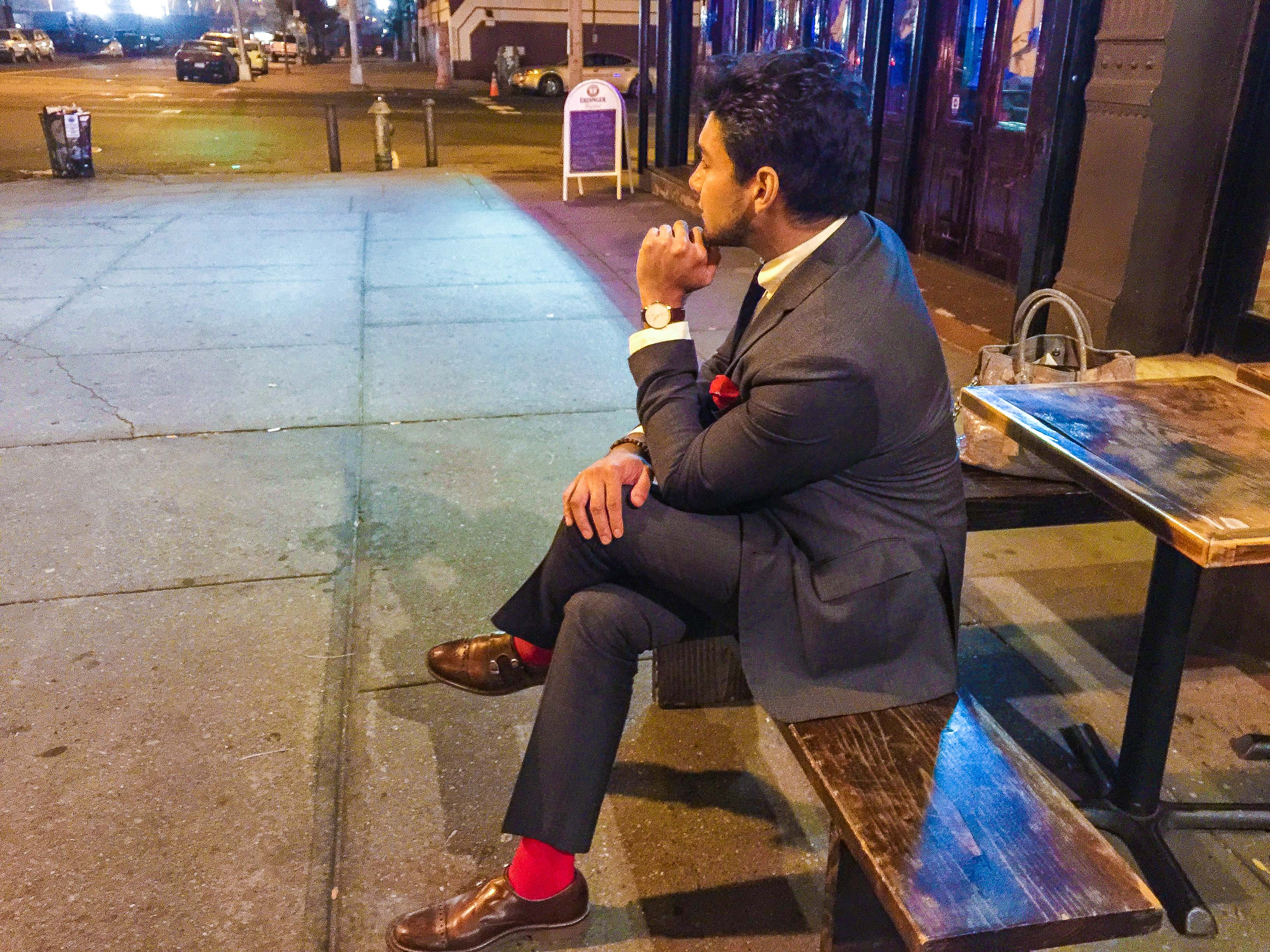 wearing a grey suit with red socks, red pocket square, brown shoes