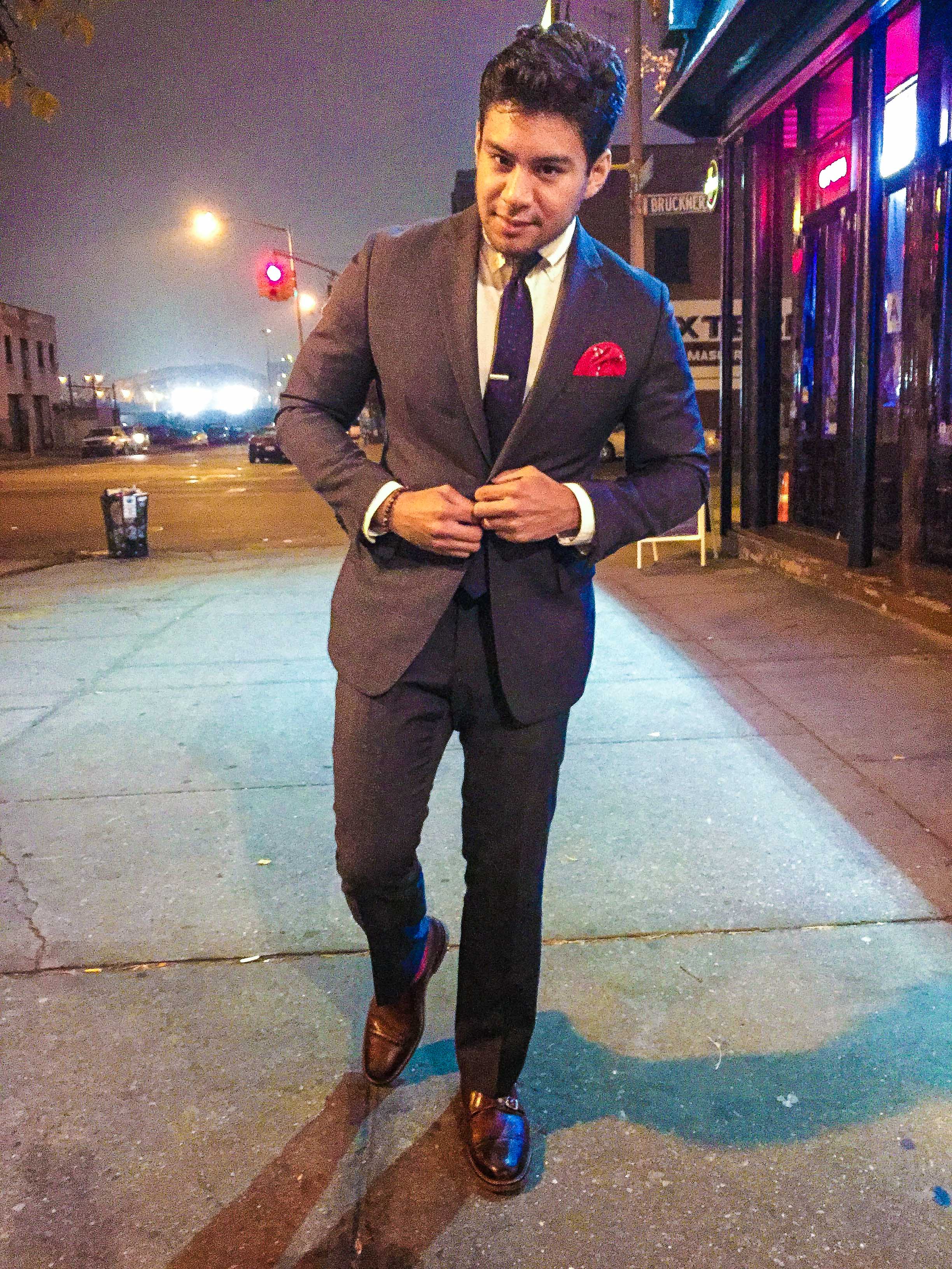 wearing a grey suit with red socks, red pocket square, brown shoes