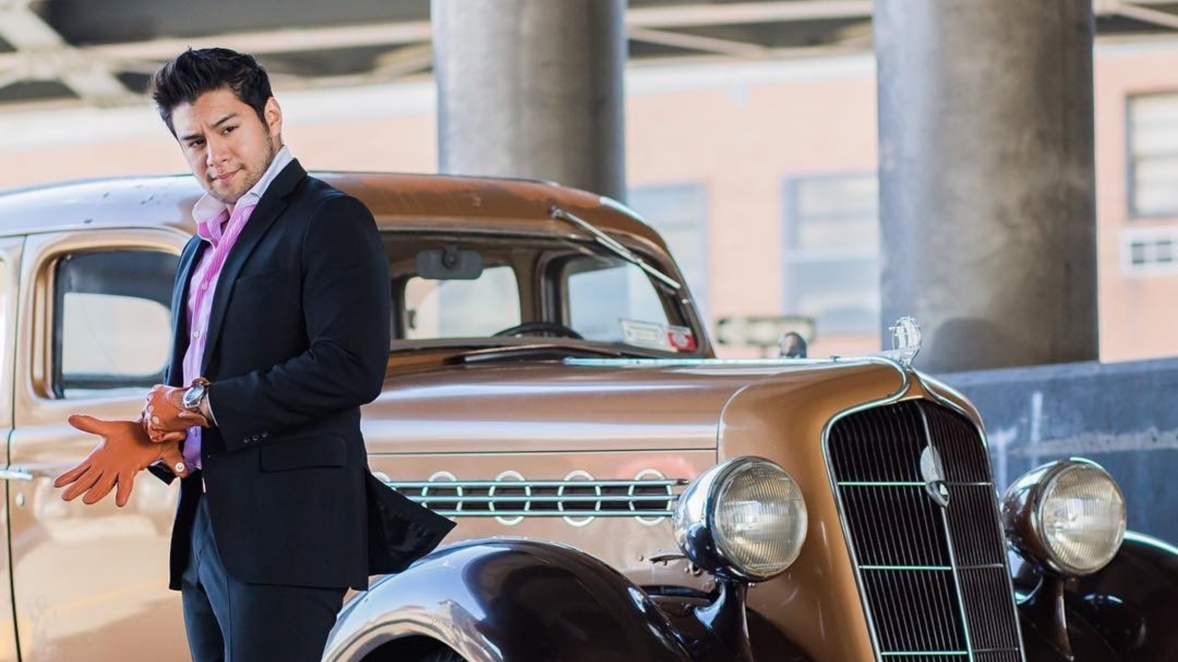 Dandy in the bronx, black suit with classic car, brown driving gloves