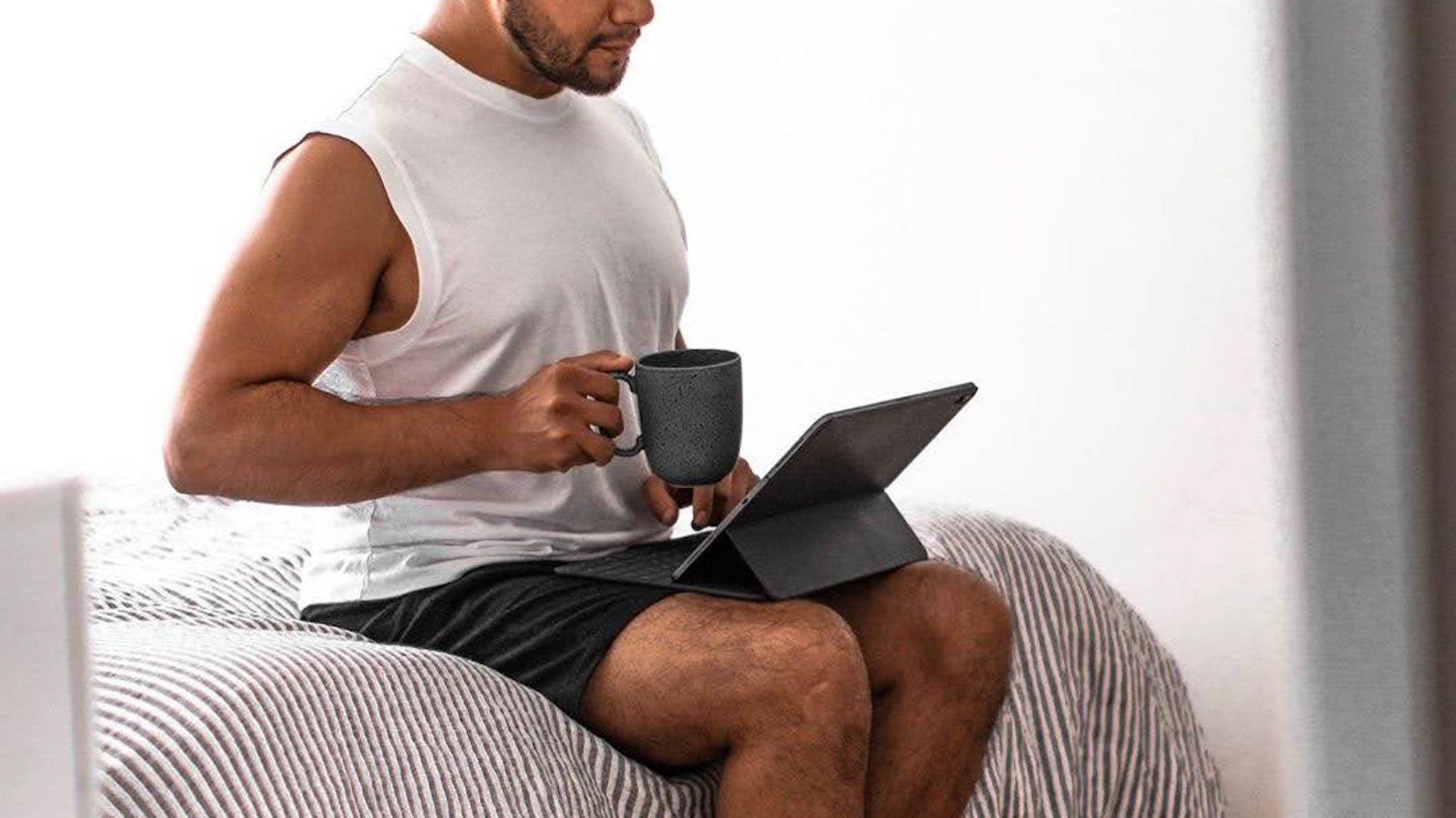 Man in shorts working from home - man holding coffee in bed - man with iPad in bed