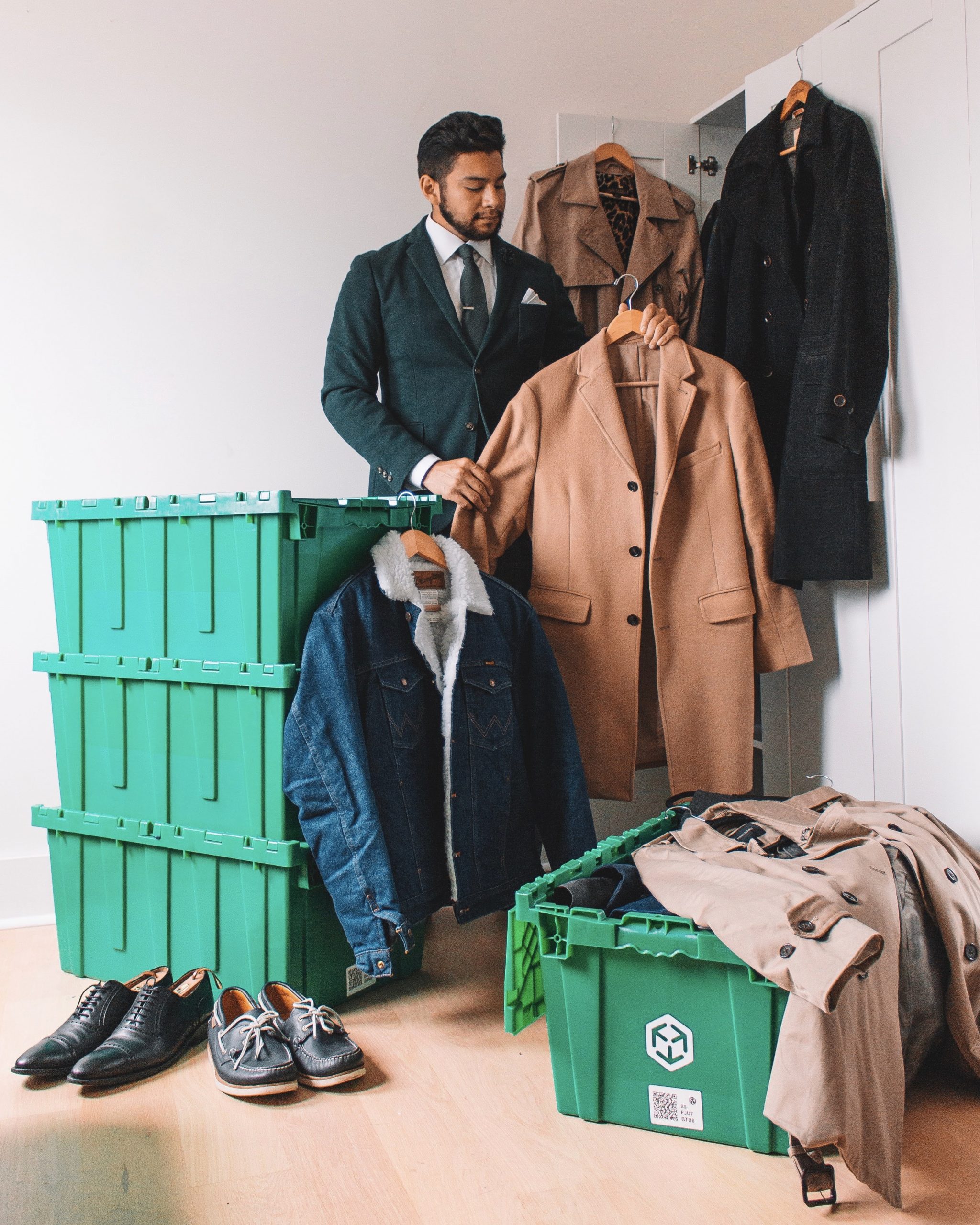 Man in green suit looking through his closet - man holding a camel coat - makespace boxes - man surrounded by coat - dandy in the Bronx