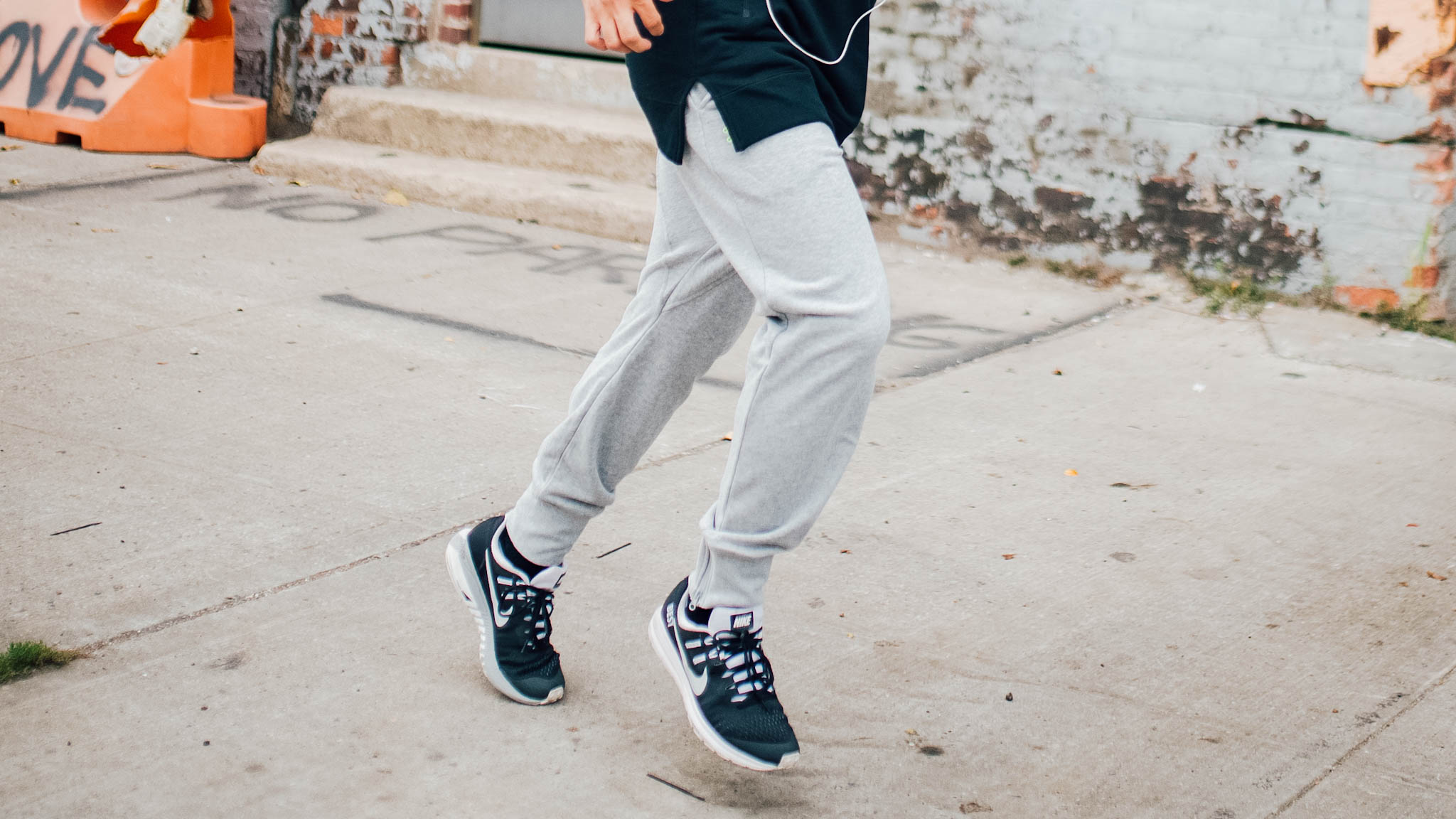man in gym clothes squatting - man in running clothes - man wearing grey joggers - grey sweat pants - black hoodie - black Nike sneakers - man running