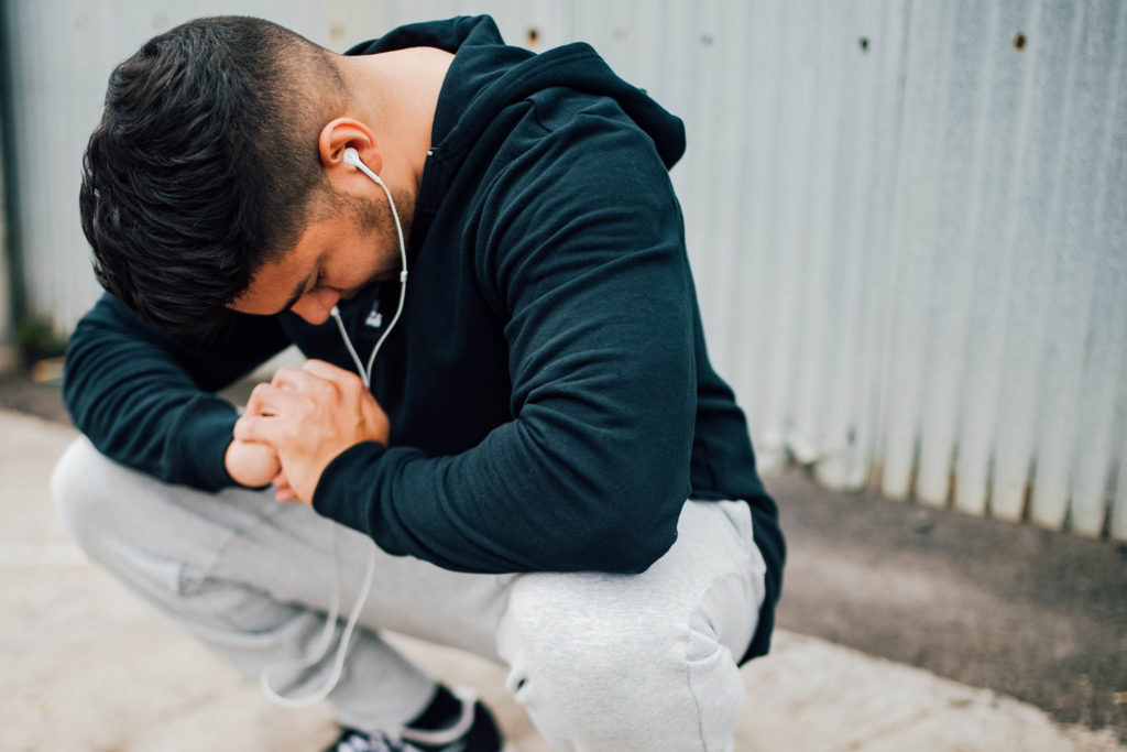 man in gym clothes squatting - man in running clothes - man wearing grey joggers - grey sweat pants - black hoodie - black Nike sneakers - man running 