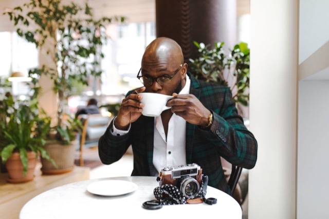 Black man wearing a plaid suit having coffee